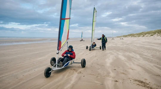 Un débutant pilote un char à voile sur une plage normande à marée basse pendant qu'un moniteur le corrige à distance.